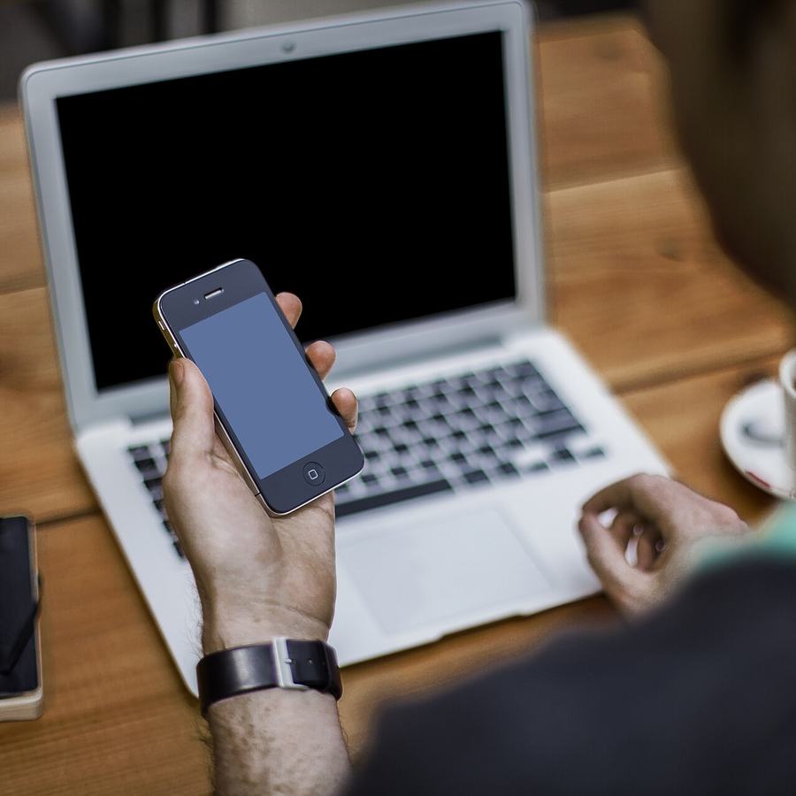 Homme qui consulte son téléphone devant un ordinateur portable